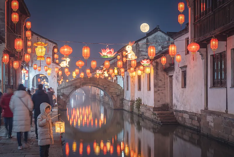 古镇元宵灯会夜景，河边挂满红色与金色灯笼，人群在灯下游赏
